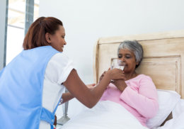 caregiver giving a glass of water to sick senior woman